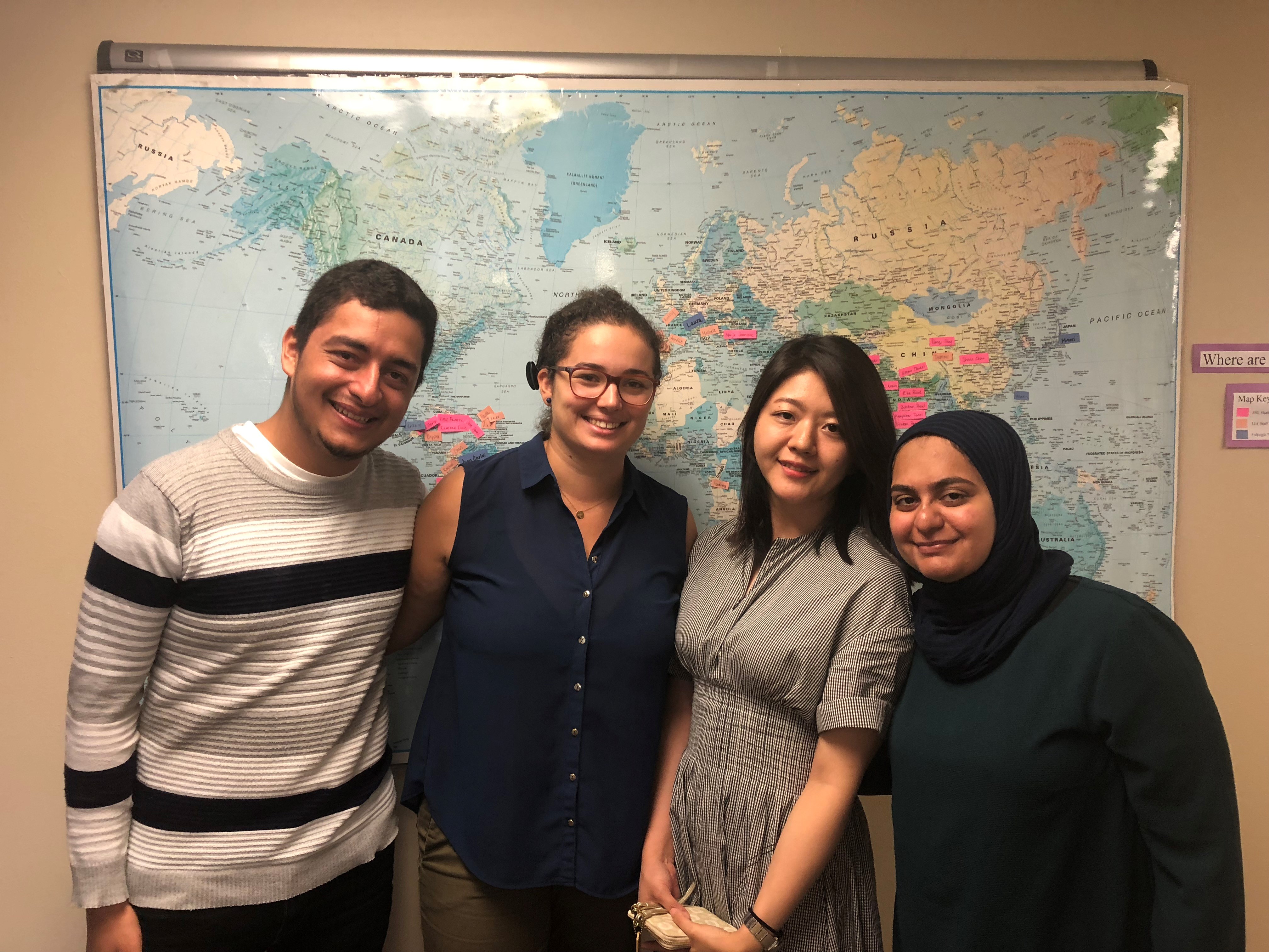 Juan Carlos Ruiz, Laura Martel, Minori Koga, and Maryam Ahmed standing in front of a world map.