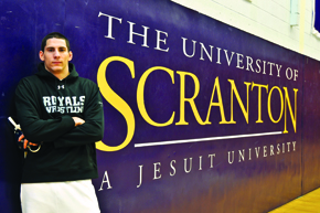 Male student standing in front of "The University of Scranton  A Jesuit University" sign on wall.